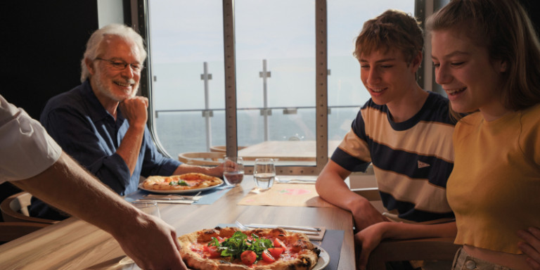 Drei Menschen am Tisch bekommen eine Pizza serviert.